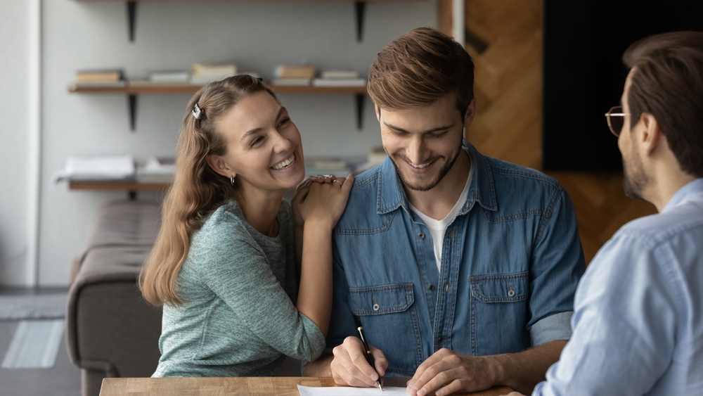 Couple signant un contrat de location avec un propriétaire, autour d'une table, atmosphère positive